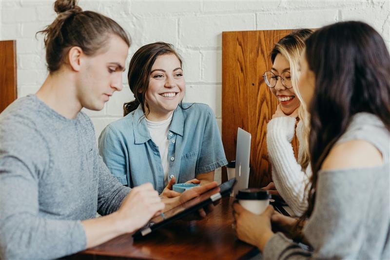 Four people speaking to each other over table with drinks and mobile devices.