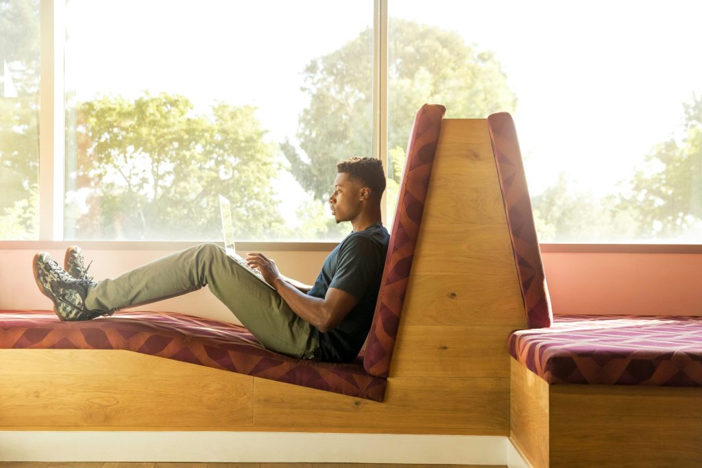 Man sitting with his feet up on a bench working on his laptop.